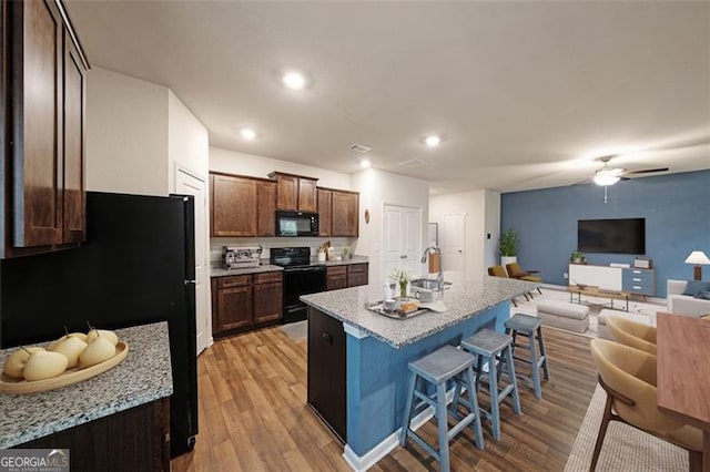 kitchen with a breakfast bar, black appliances, light hardwood / wood-style flooring, ceiling fan, and an island with sink