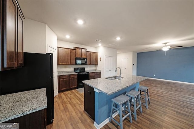 kitchen with a kitchen island with sink, black appliances, a kitchen breakfast bar, sink, and light hardwood / wood-style flooring