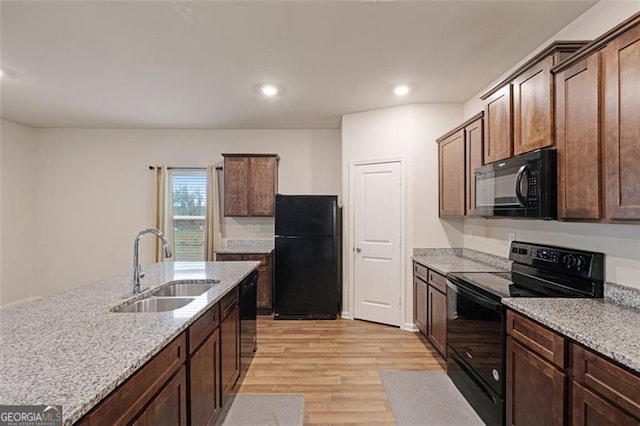 kitchen featuring light stone countertops, sink, light hardwood / wood-style floors, and black appliances