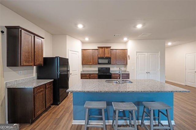 kitchen featuring light stone countertops, a kitchen island with sink, black appliances, and light wood-type flooring