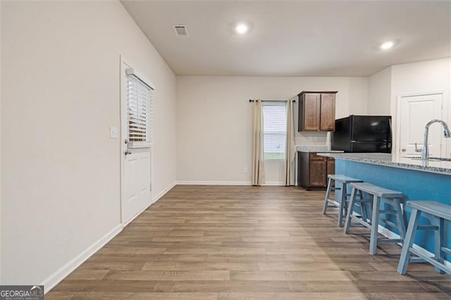 kitchen featuring a kitchen bar, black fridge, sink, light hardwood / wood-style floors, and light stone counters