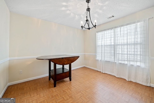 dining room with a textured ceiling, a notable chandelier, and light parquet flooring