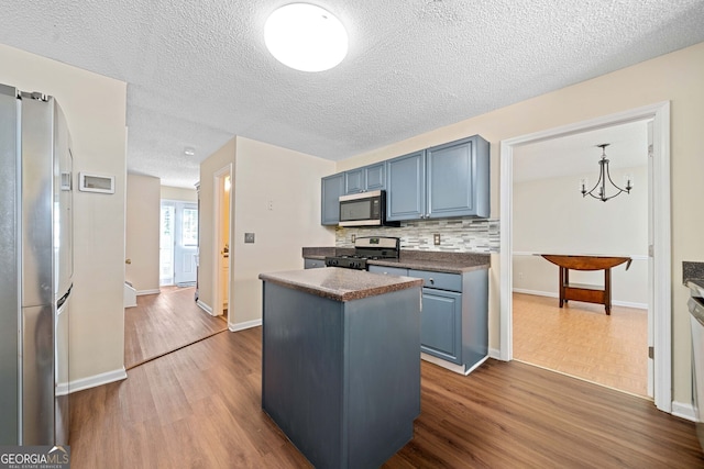 kitchen featuring dark wood-type flooring, stainless steel appliances, pendant lighting, a textured ceiling, and a kitchen island