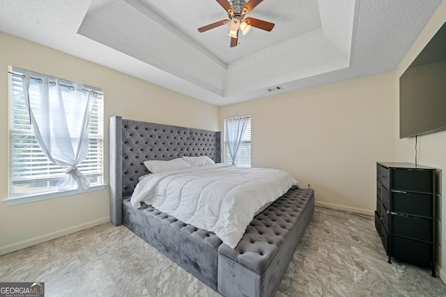 bedroom with a textured ceiling, a raised ceiling, multiple windows, and ceiling fan