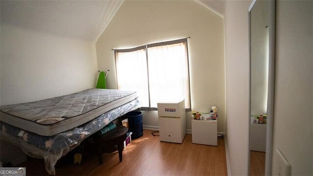 bedroom featuring light wood-type flooring, white refrigerator, and vaulted ceiling