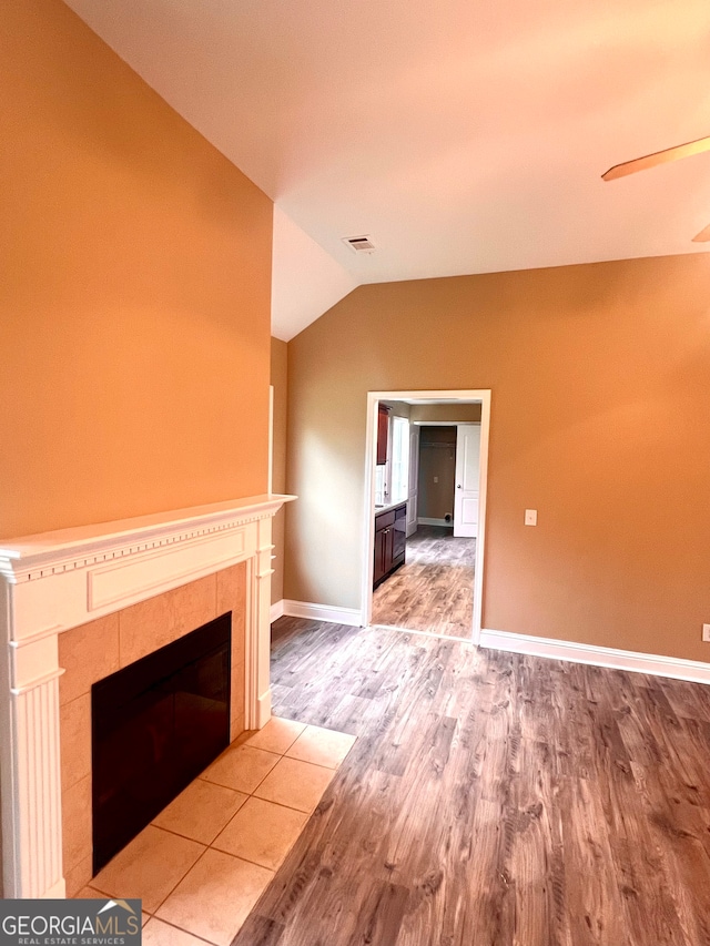 unfurnished living room featuring a tile fireplace, hardwood / wood-style floors, and vaulted ceiling