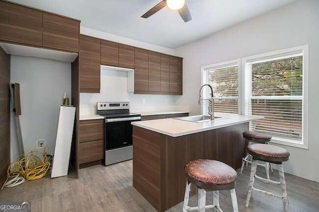 kitchen featuring stainless steel range with electric stovetop, sink, light wood-type flooring, an island with sink, and a kitchen bar