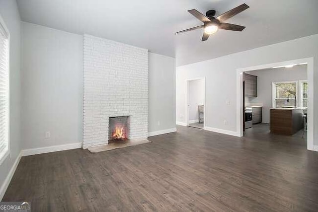 unfurnished living room featuring ceiling fan, dark hardwood / wood-style flooring, and a brick fireplace