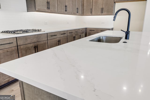 kitchen featuring backsplash, light stone counters, stainless steel gas cooktop, and sink