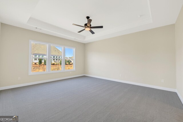 spare room featuring dark colored carpet, a tray ceiling, and ceiling fan