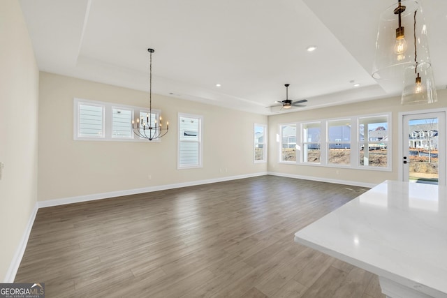 unfurnished living room featuring ceiling fan with notable chandelier, hardwood / wood-style flooring, and a raised ceiling