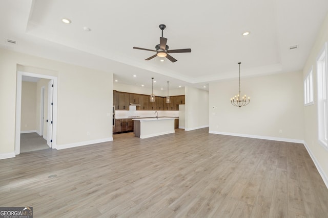 unfurnished living room with a tray ceiling, ceiling fan with notable chandelier, and light wood-type flooring