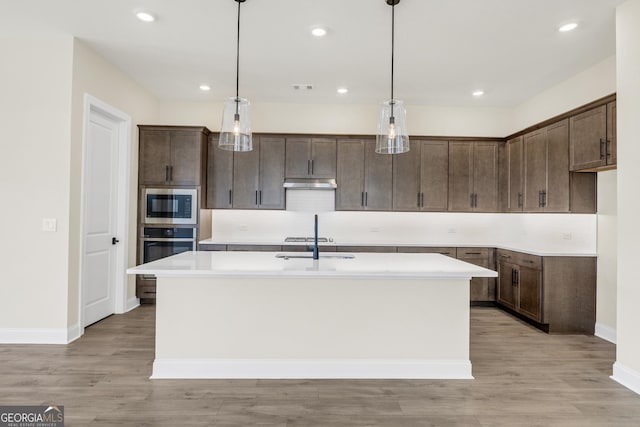 kitchen featuring decorative light fixtures, light hardwood / wood-style floors, and an island with sink