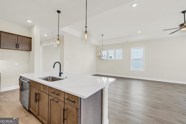 kitchen with light wood-type flooring, stainless steel dishwasher, sink, hanging light fixtures, and an island with sink