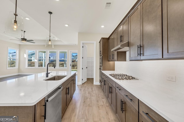 kitchen with appliances with stainless steel finishes, light wood-type flooring, ceiling fan, sink, and decorative light fixtures