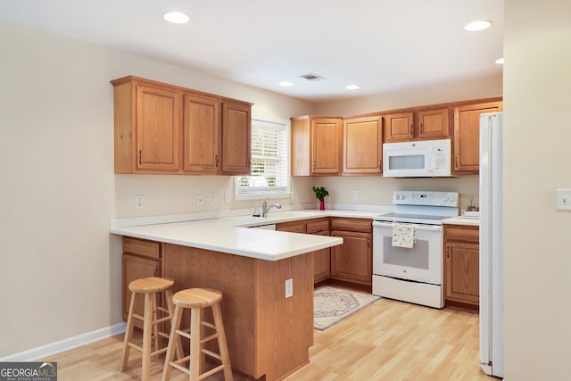 kitchen with white appliances, sink, light hardwood / wood-style floors, a kitchen bar, and kitchen peninsula