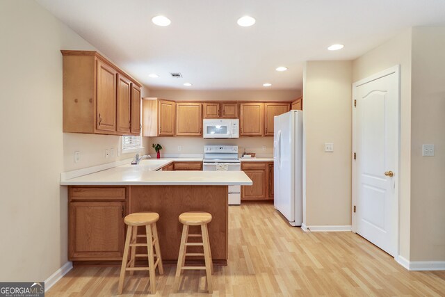 kitchen with kitchen peninsula, light wood-type flooring, a breakfast bar, white appliances, and sink