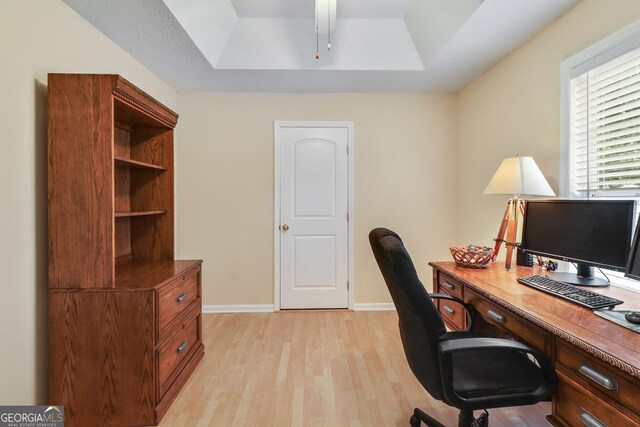 home office featuring a raised ceiling and light hardwood / wood-style flooring