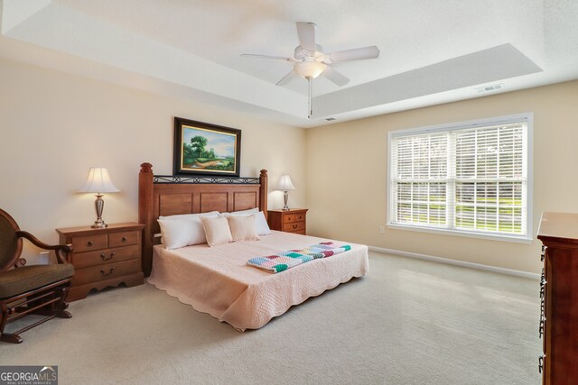 carpeted bedroom with a tray ceiling and ceiling fan