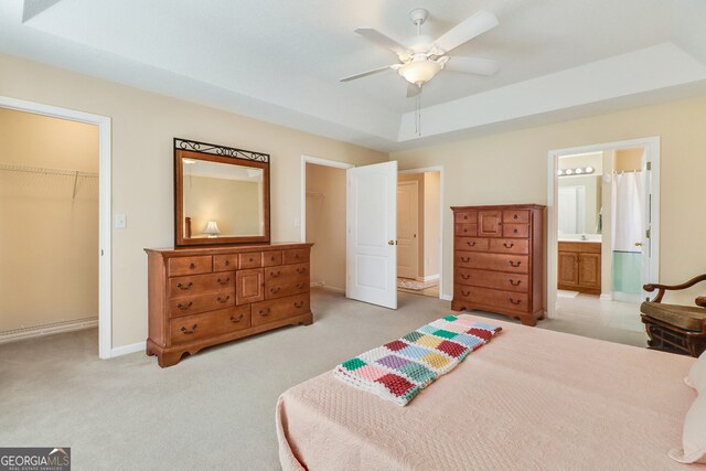 carpeted bedroom featuring a raised ceiling, ensuite bath, ceiling fan, a spacious closet, and a closet