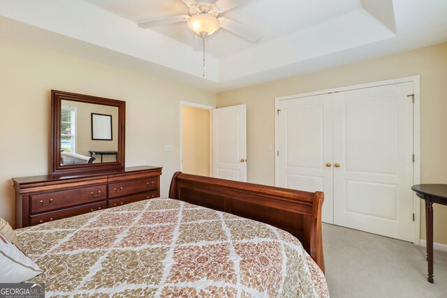 bedroom featuring light carpet, a closet, a raised ceiling, and ceiling fan