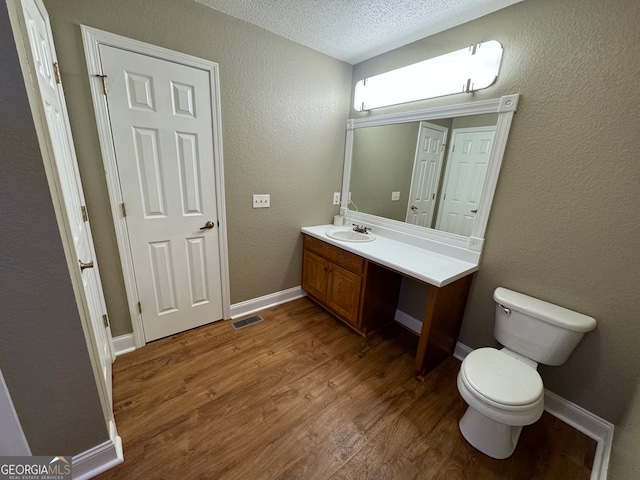 bathroom featuring vanity, wood-type flooring, a textured ceiling, and toilet