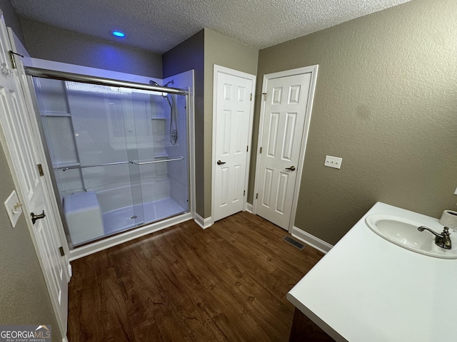 full bath featuring a stall shower, vanity, a textured wall, and wood finished floors