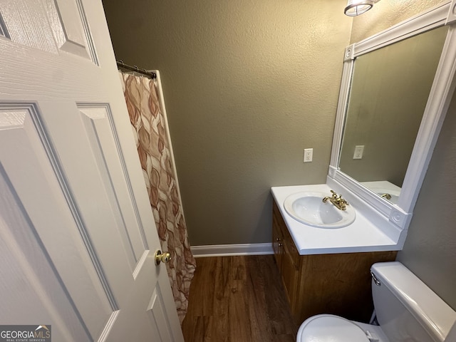 full bathroom featuring vanity, wood finished floors, baseboards, toilet, and a textured wall