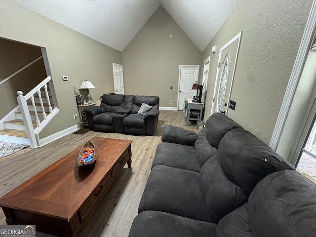 living area with high vaulted ceiling, wood finished floors, baseboards, a healthy amount of sunlight, and stairs