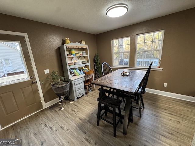 dining space featuring light wood finished floors, a textured ceiling, baseboards, and a textured wall
