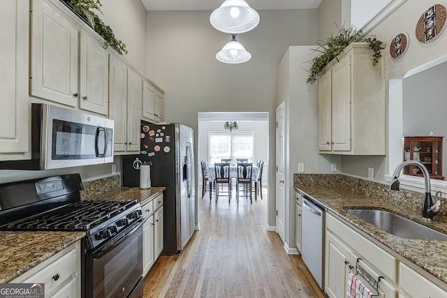 kitchen featuring appliances with stainless steel finishes, light hardwood / wood-style floors, dark stone countertops, and sink