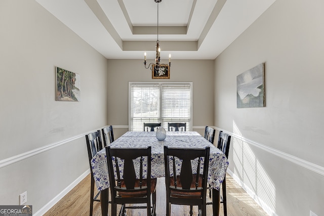 dining room featuring a notable chandelier, light hardwood / wood-style floors, and a tray ceiling