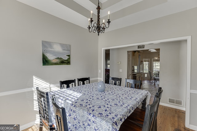 dining area with a raised ceiling, dark hardwood / wood-style floors, and an inviting chandelier