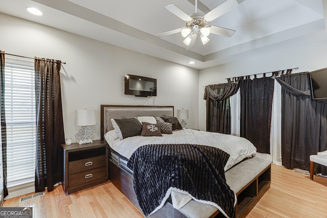 bedroom with ceiling fan, a raised ceiling, and light hardwood / wood-style flooring