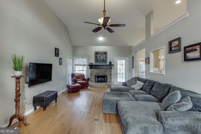 living room featuring ceiling fan, a fireplace, high vaulted ceiling, and light wood-type flooring