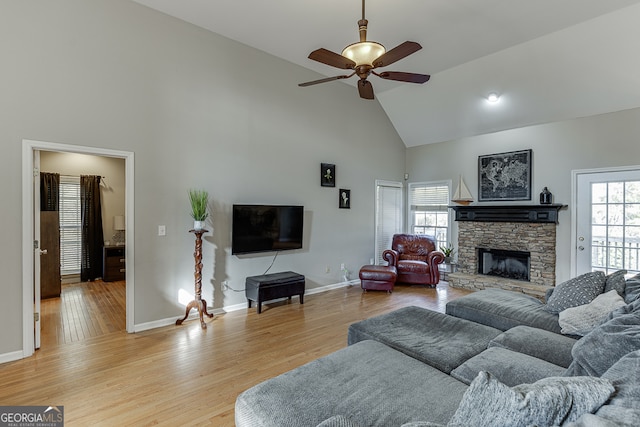 living room featuring a stone fireplace, ceiling fan, light hardwood / wood-style flooring, and high vaulted ceiling