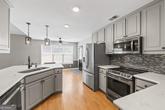 kitchen featuring light wood-style flooring, a sink, stainless steel appliances, gray cabinetry, and backsplash