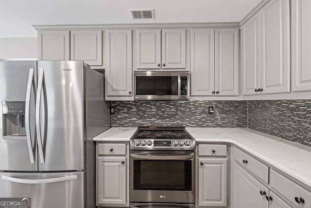 kitchen with appliances with stainless steel finishes, visible vents, decorative backsplash, and light stone countertops