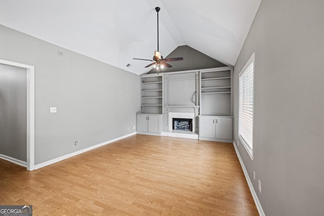 unfurnished living room with light wood finished floors, baseboards, a ceiling fan, a premium fireplace, and vaulted ceiling