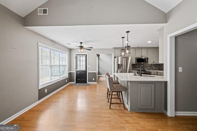 kitchen with lofted ceiling, stainless steel appliances, visible vents, gray cabinets, and light wood finished floors