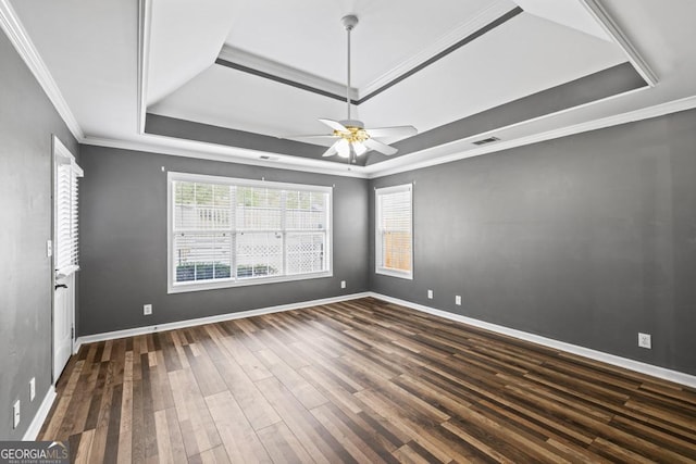 empty room with baseboards, visible vents, a tray ceiling, and wood finished floors