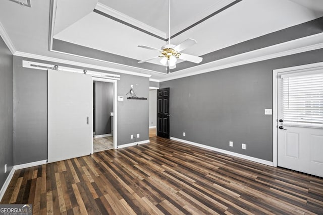 unfurnished bedroom with a raised ceiling, a barn door, ornamental molding, wood finished floors, and baseboards