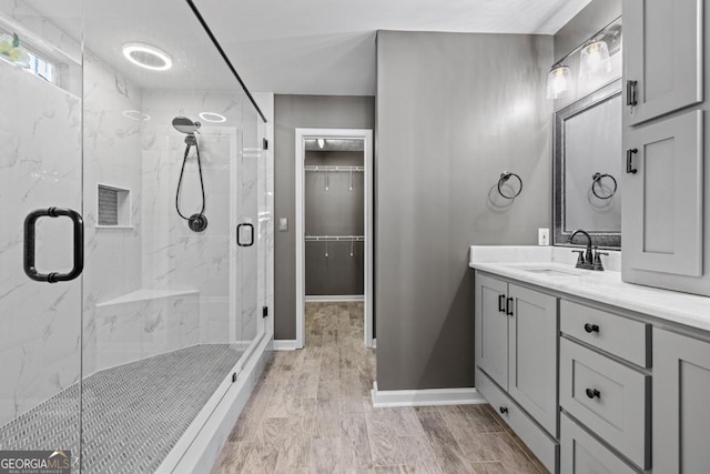 bathroom featuring a marble finish shower, baseboards, wood tiled floor, a walk in closet, and vanity