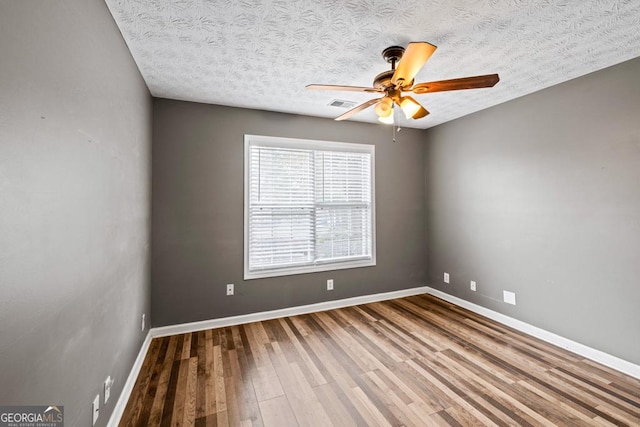 empty room with baseboards, visible vents, a ceiling fan, wood finished floors, and a textured ceiling