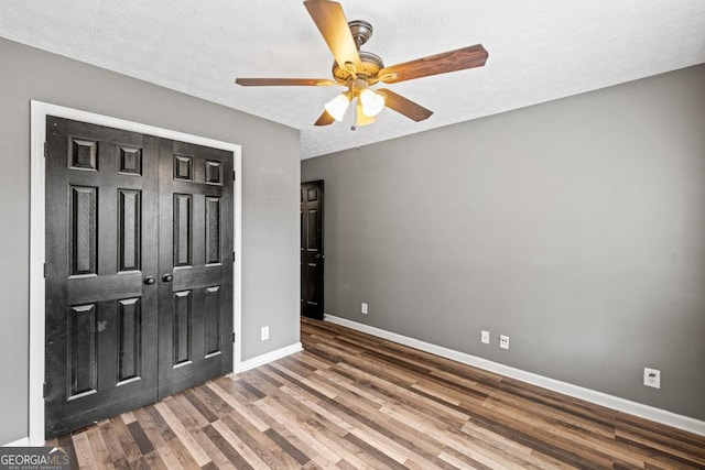 unfurnished bedroom with a textured ceiling, ceiling fan, wood finished floors, baseboards, and a closet