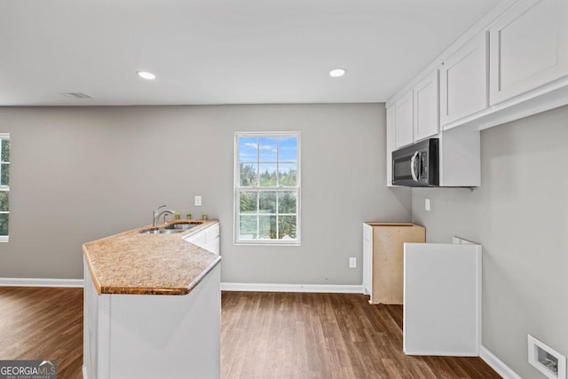 kitchen with visible vents, baseboards, stainless steel microwave, a peninsula, and white cabinetry