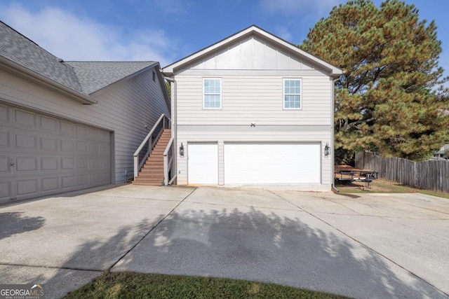 view of side of home with concrete driveway, stairway, board and batten siding, and fence