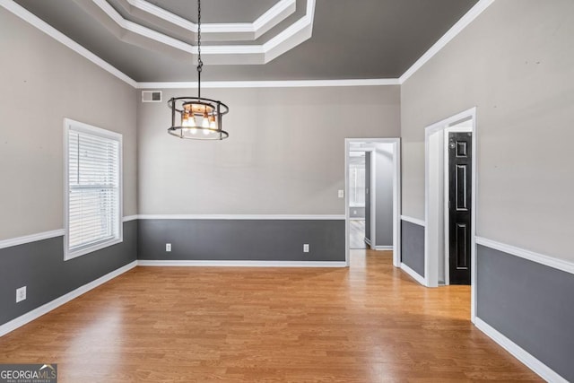 empty room featuring a chandelier, wood finished floors, baseboards, ornamental molding, and a tray ceiling