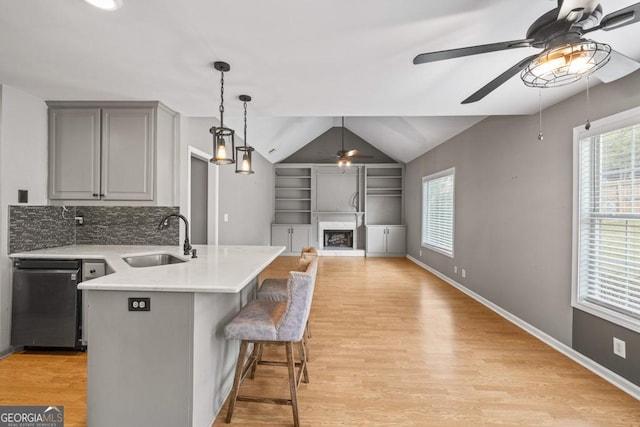 kitchen with a fireplace with raised hearth, light countertops, gray cabinetry, light wood-type flooring, and a sink