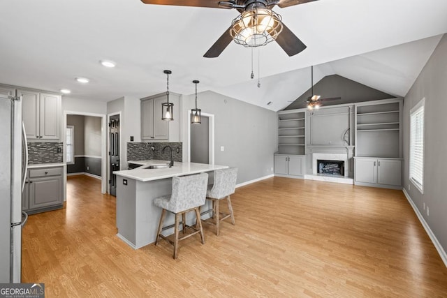 kitchen with a breakfast bar area, a peninsula, light wood-style floors, gray cabinets, and freestanding refrigerator